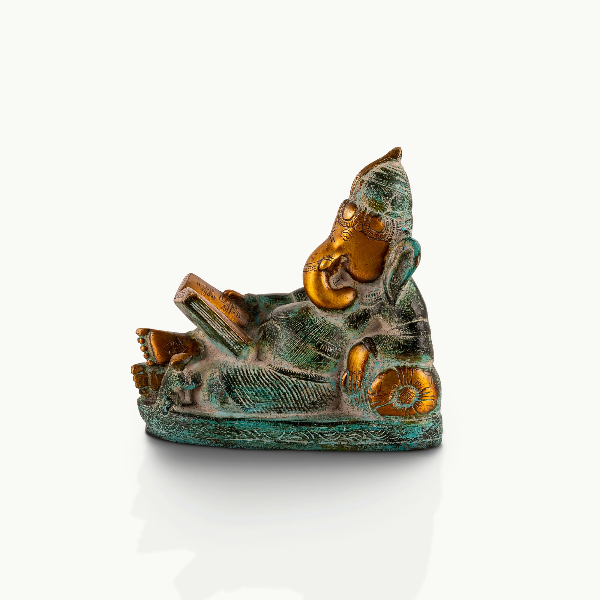 Reading Ganesha Brass Statue reclining gracefully against a pillow on an executive desk. 