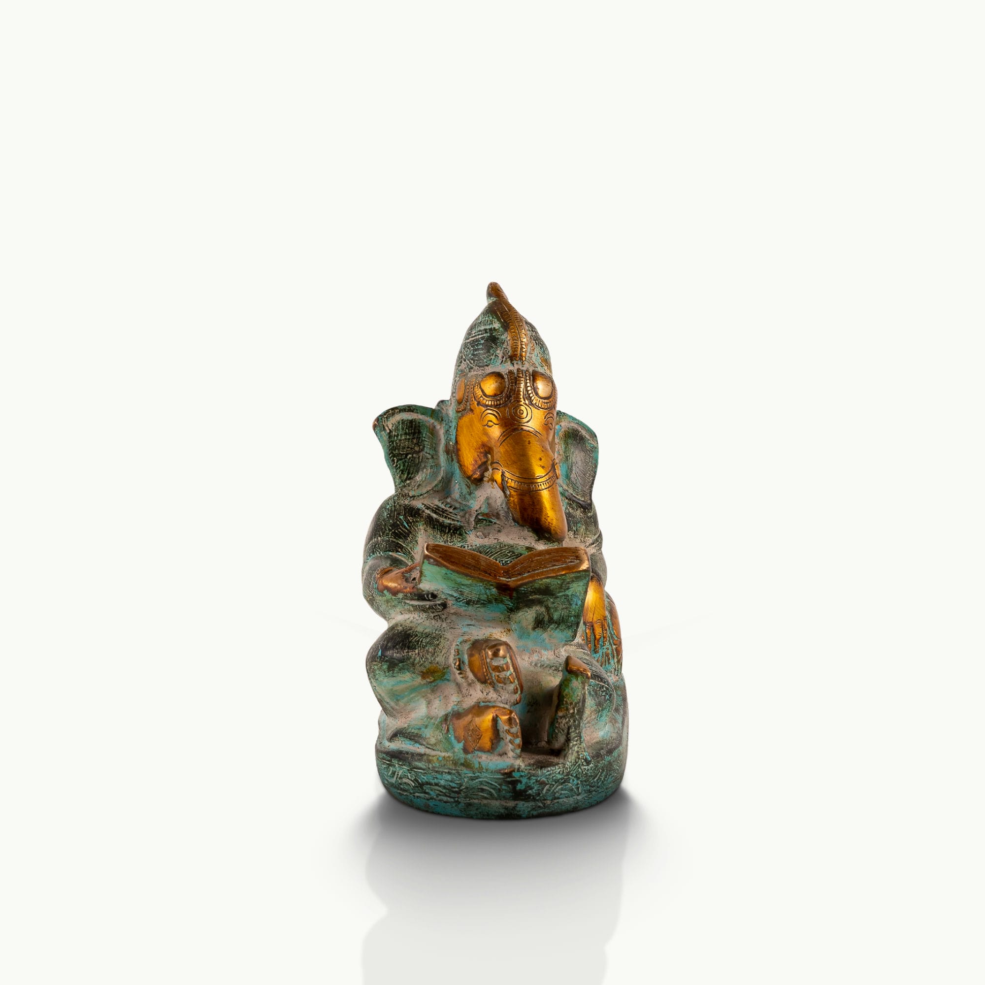 Reading Ganesha Brass Statue reclining gracefully against a pillow on an executive desk. 