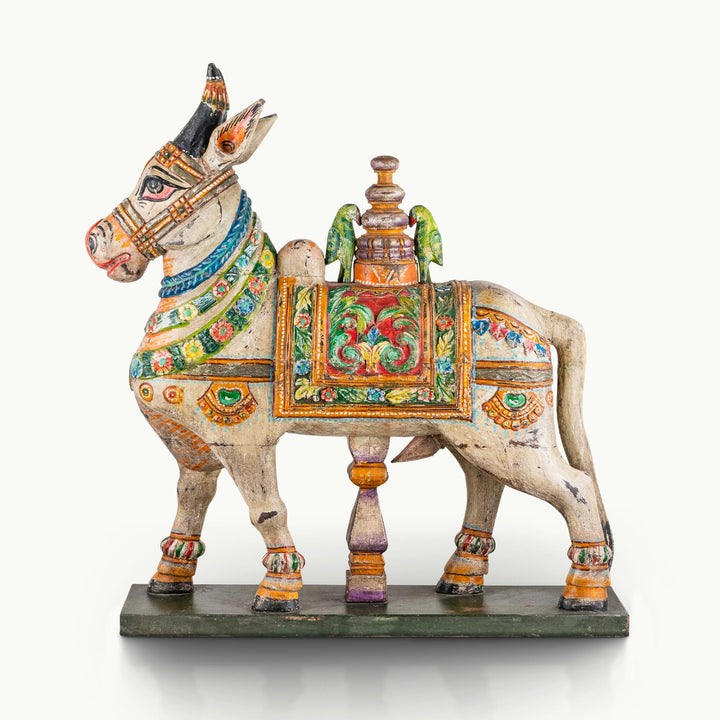 Painted wooden Nandi sculpture with a distressed whitewashed body and vibrant floral blanket.