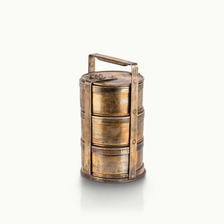 Antique brass tiffin carrier featuring three stacked tiers and a riveted metal frame.