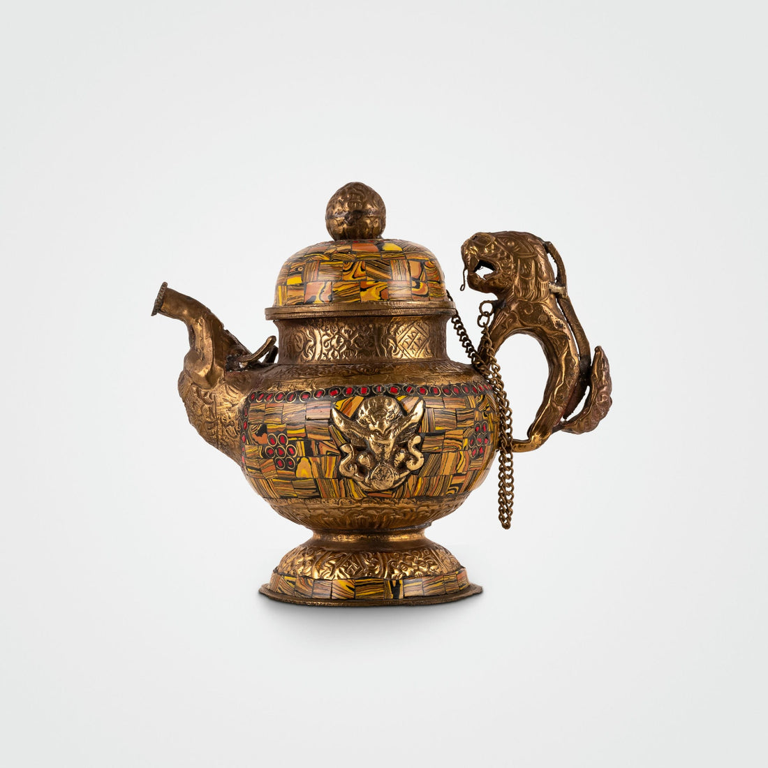 Stone chip inlay brass teapot featuring amber mosaics and a lion handle, positioned as a centerpiece for a glass curio cabinet. 