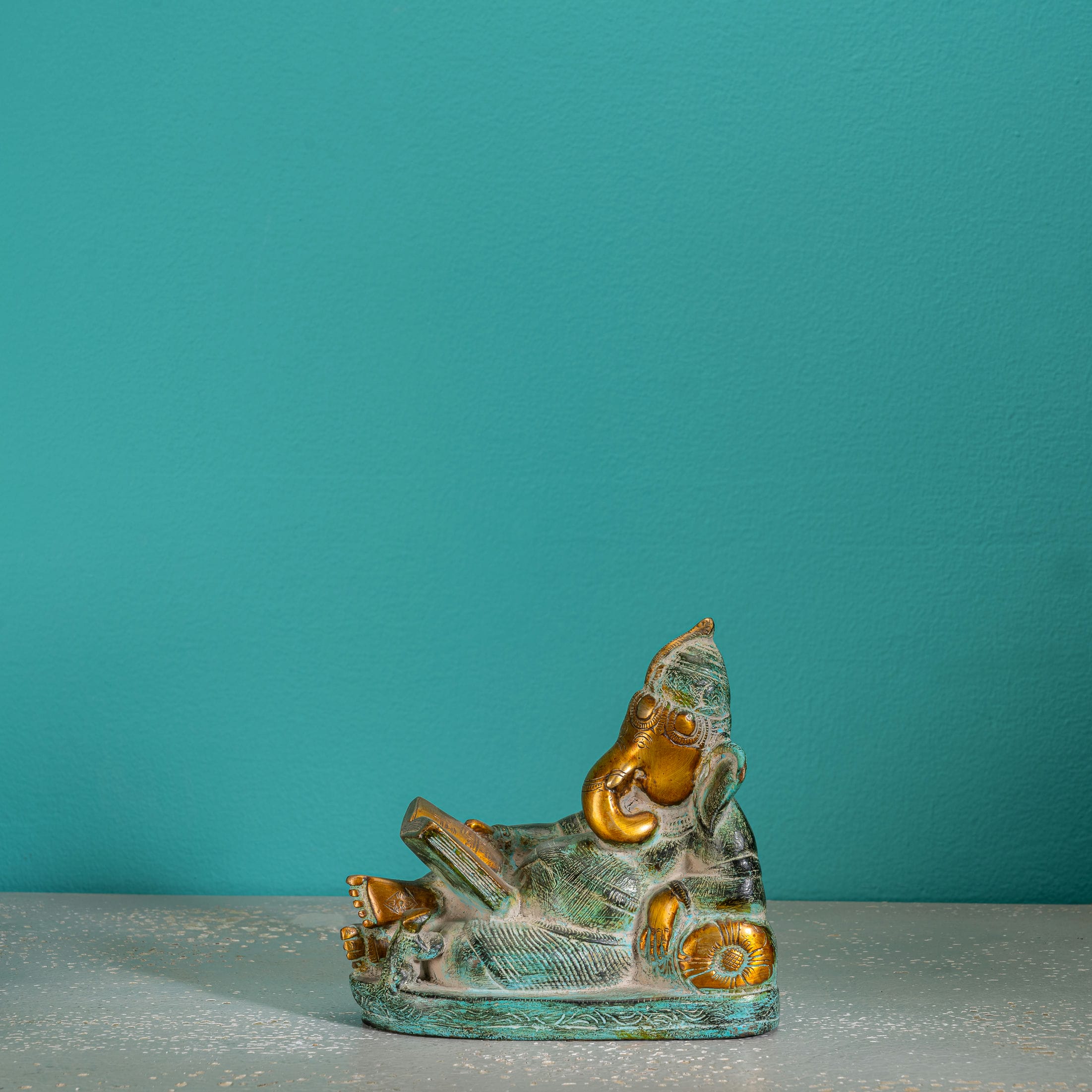 Reading Ganesha Brass Statue reclining gracefully against a pillow on an executive desk. 