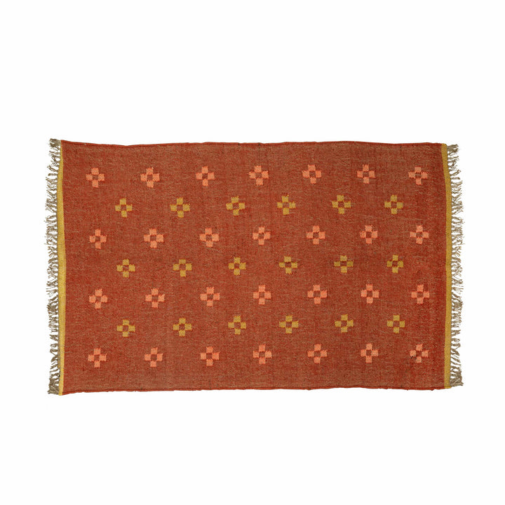 Flatweave terracotta wool jute rug in a living room, with stepped geometric crosses in peach and coral. 