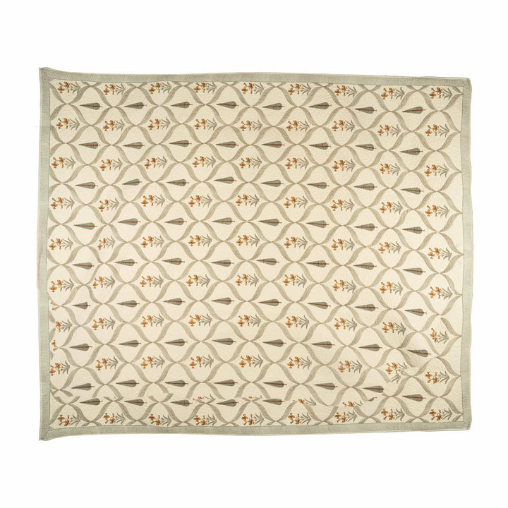 Amber block-print cotton bedcover folded, showcasing warm floral sprigs and sage-green foliage for an inviting guest room.
