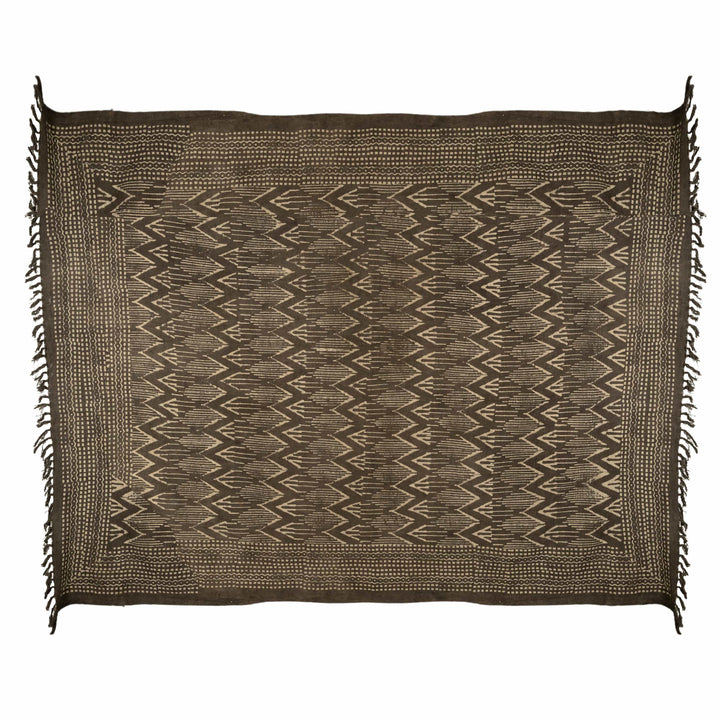 Brown ikat cotton bedcover folded, showcasing natural cream chevrons and thick knotted fringes for a rustic master suite.