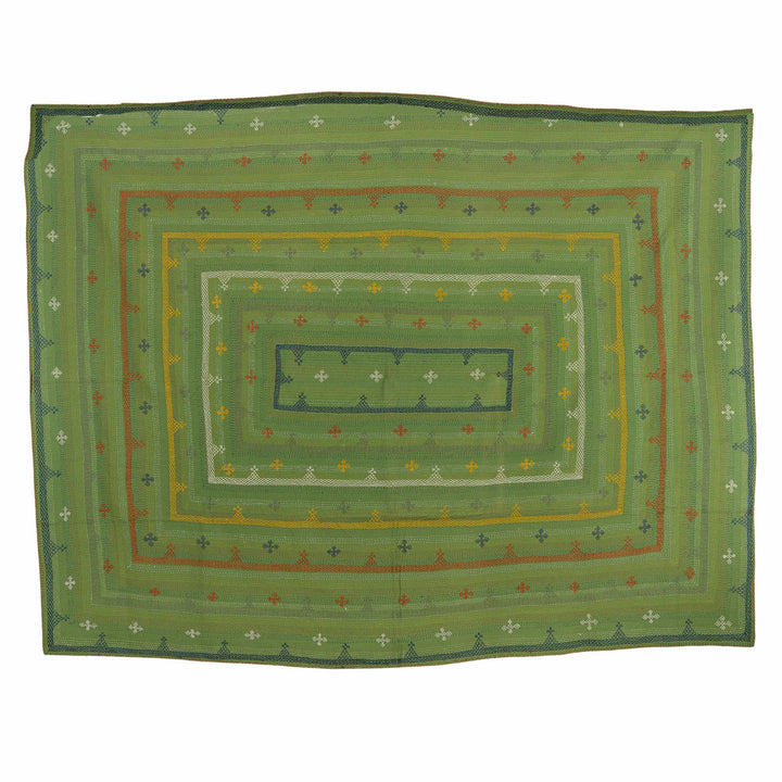 Green geometric kantha bedcover draped across a vibrant guest bedroom featuring intricate multi-coloured hand-embroidered frames.