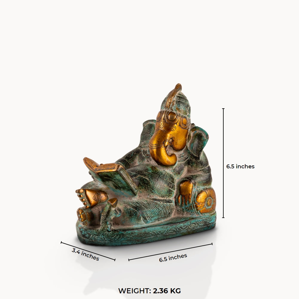 Reading Ganesha Brass Statue reclining gracefully against a pillow on an executive desk. 